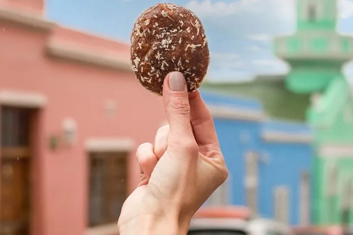 A coconut-dusted pastry held up in front of coloured houses